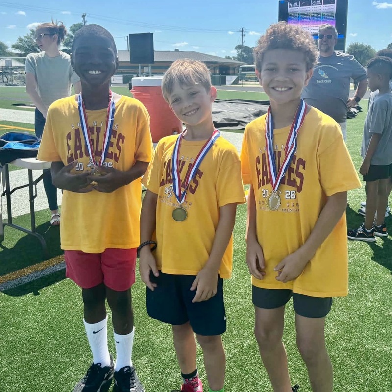 Three second grade boys wearing medals stand side-by-side.