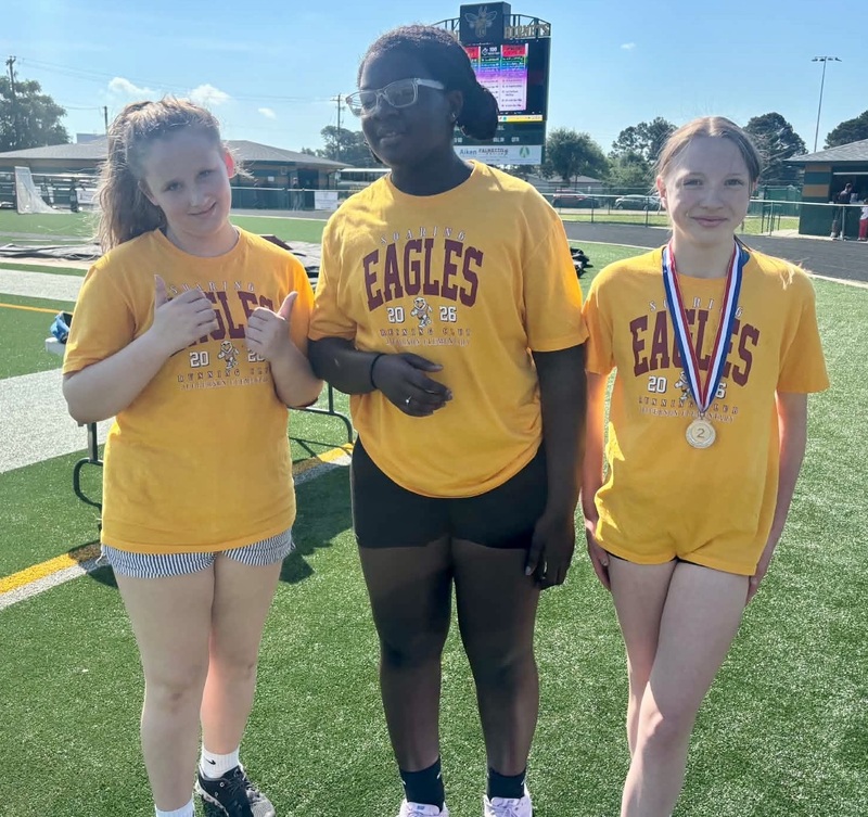 Three girls, one wearing a medal, stand side-by-side.