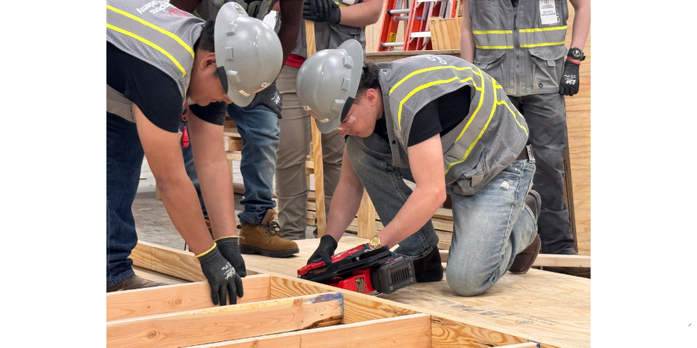 TWO STUDENTS HELPING EACH OTHER BUILD A HOUSE FRAME INDOORS