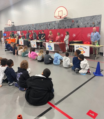 students sitting on floor while adults are talking
