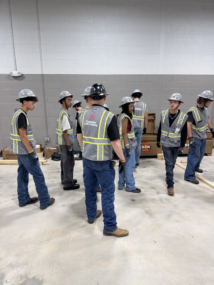 Students in an industrial setting, wearing a vest and hardhats