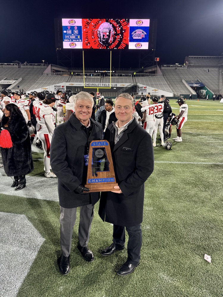 Two people holding a trophy on a football field