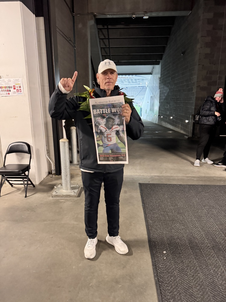 A coach holding a trophy and holding a number one symbol with his right arm