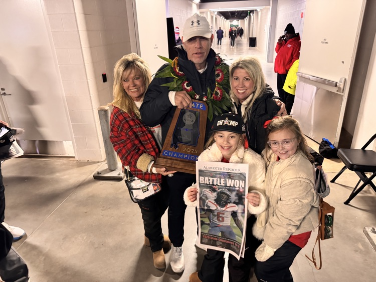 A family holding a trophy, smiling in a stadium interior corridor after a game