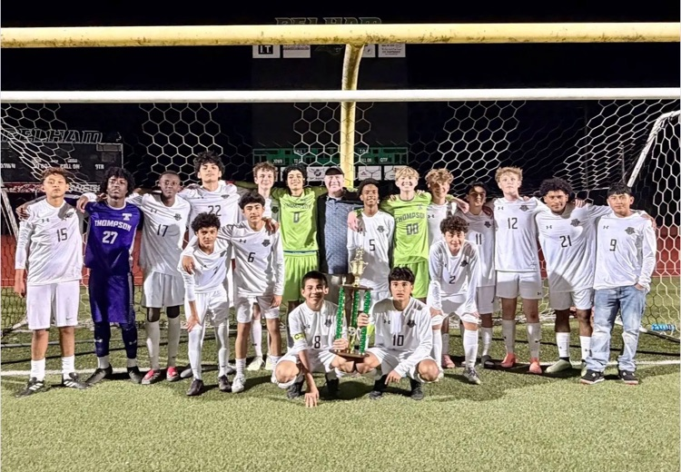 Group of soccer players posing for a photo in front of a soccer net on a field