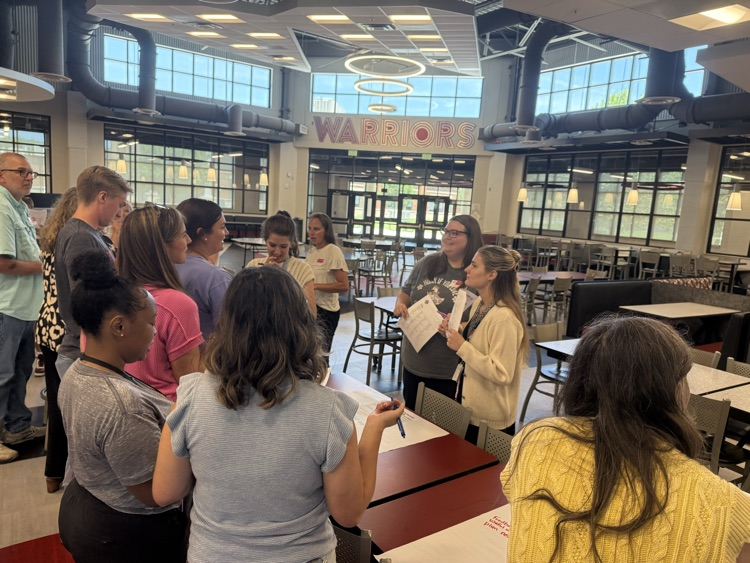 Teachers engage in a collaborative exercise inside of a high school cafeteria
