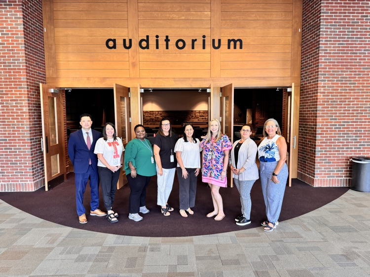 eight people posing in front of sign that says “Auditorium"