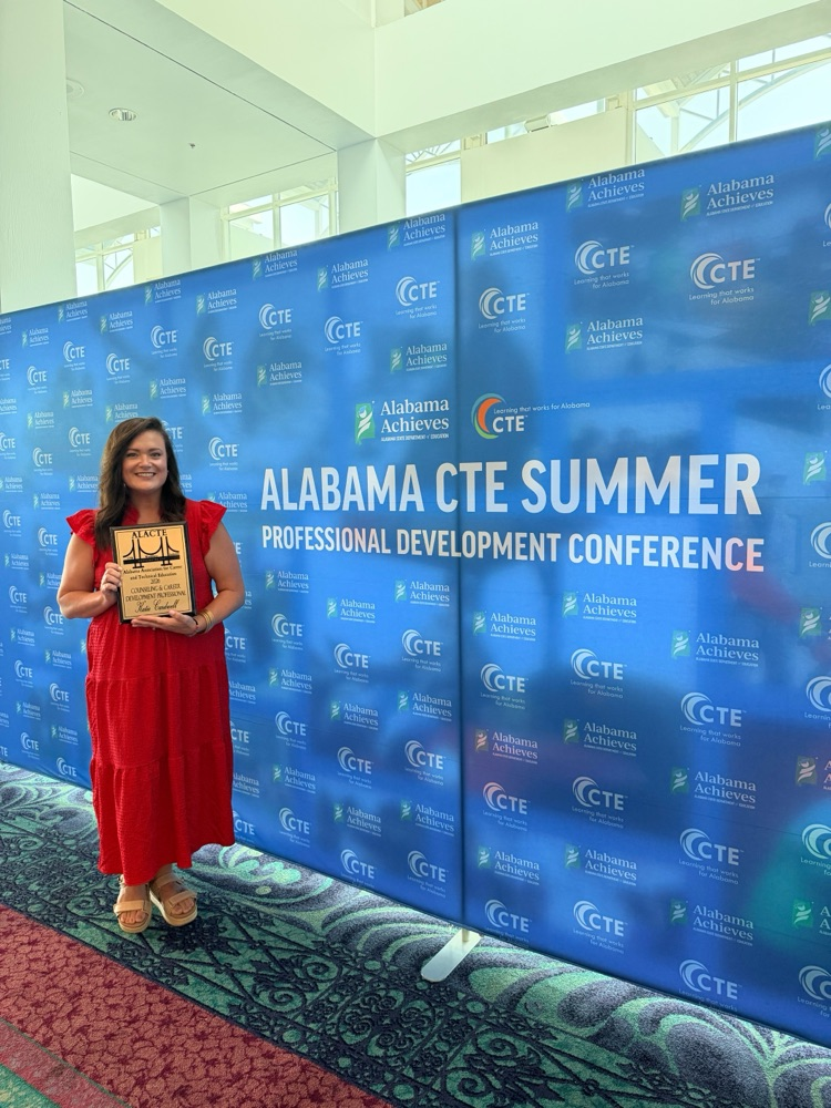 Woman in red dress, holding an award in front of step repeat banner in hotel lobby
