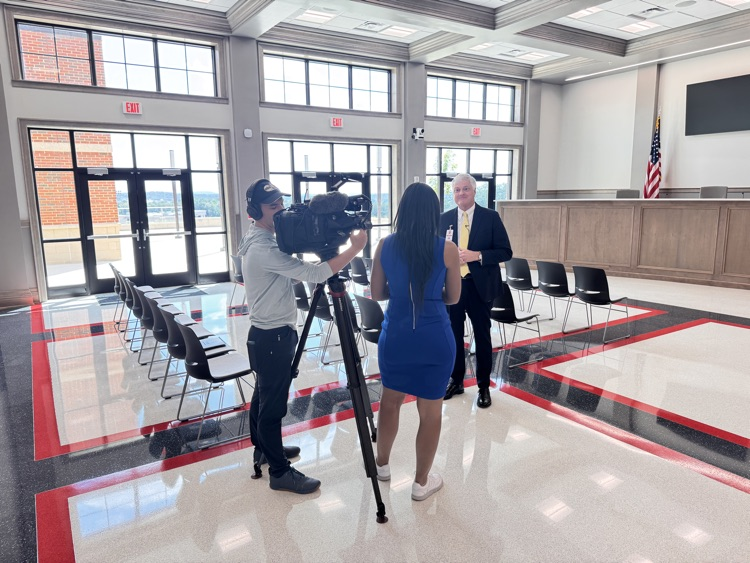 Man being interviewed by TV CREW in well-lit Board of Education Chambers