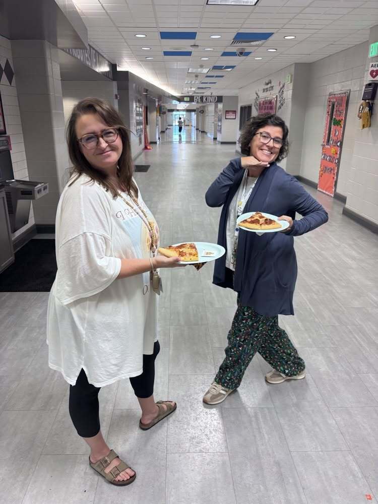 two teachers holding plates with slices of pizza on them