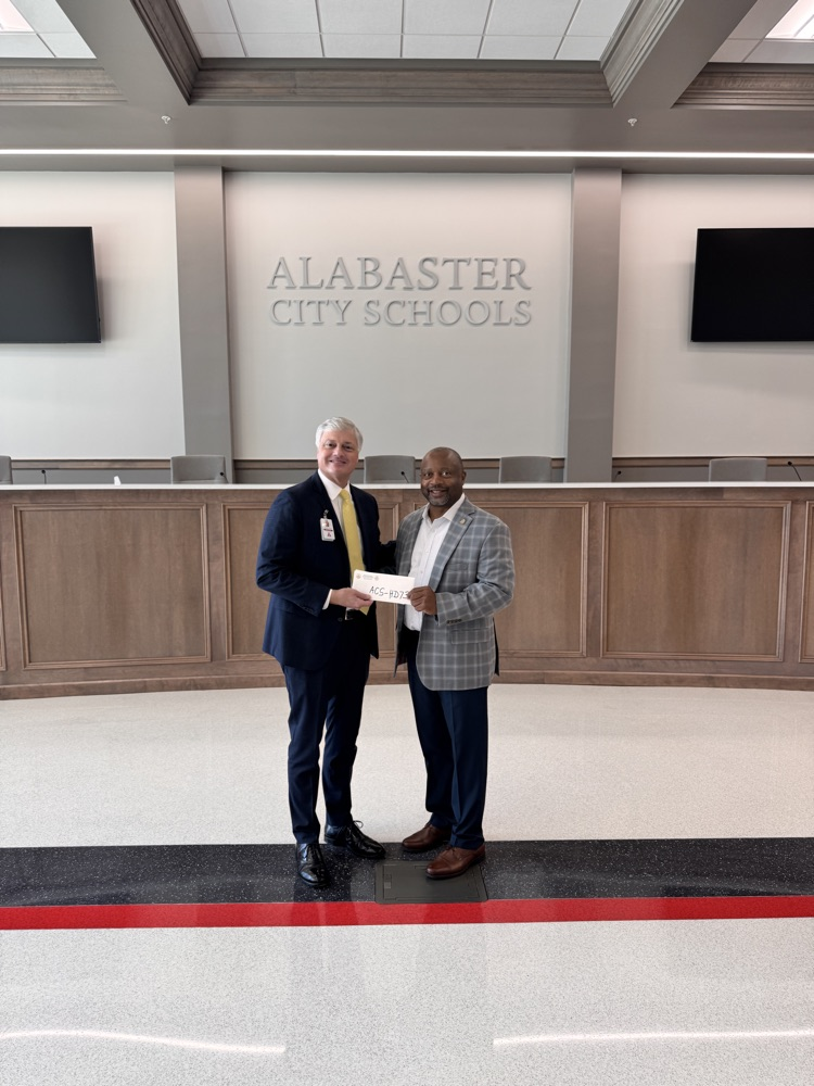 two men in a large board room holding a check 
