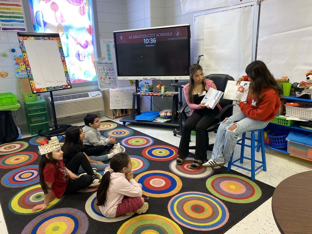 two students in chairs reading to smaller chilren