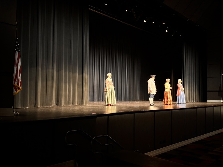 actors on stage with dark curtain behind them