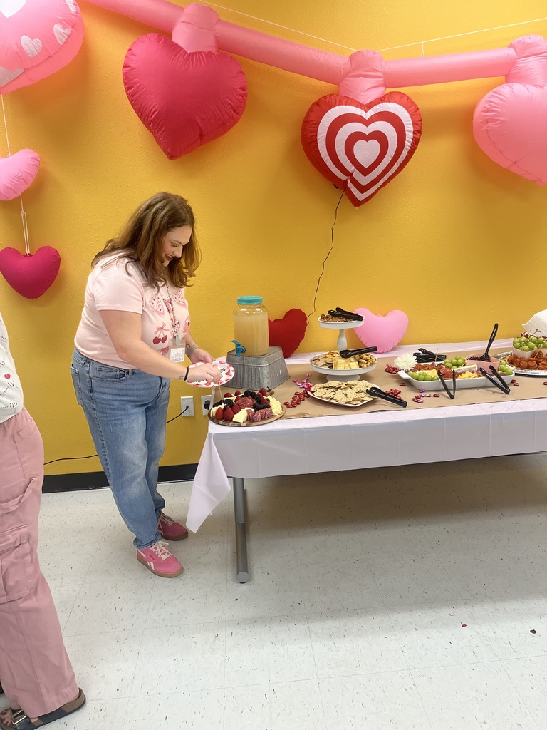 teacher in front of heart balloons and table