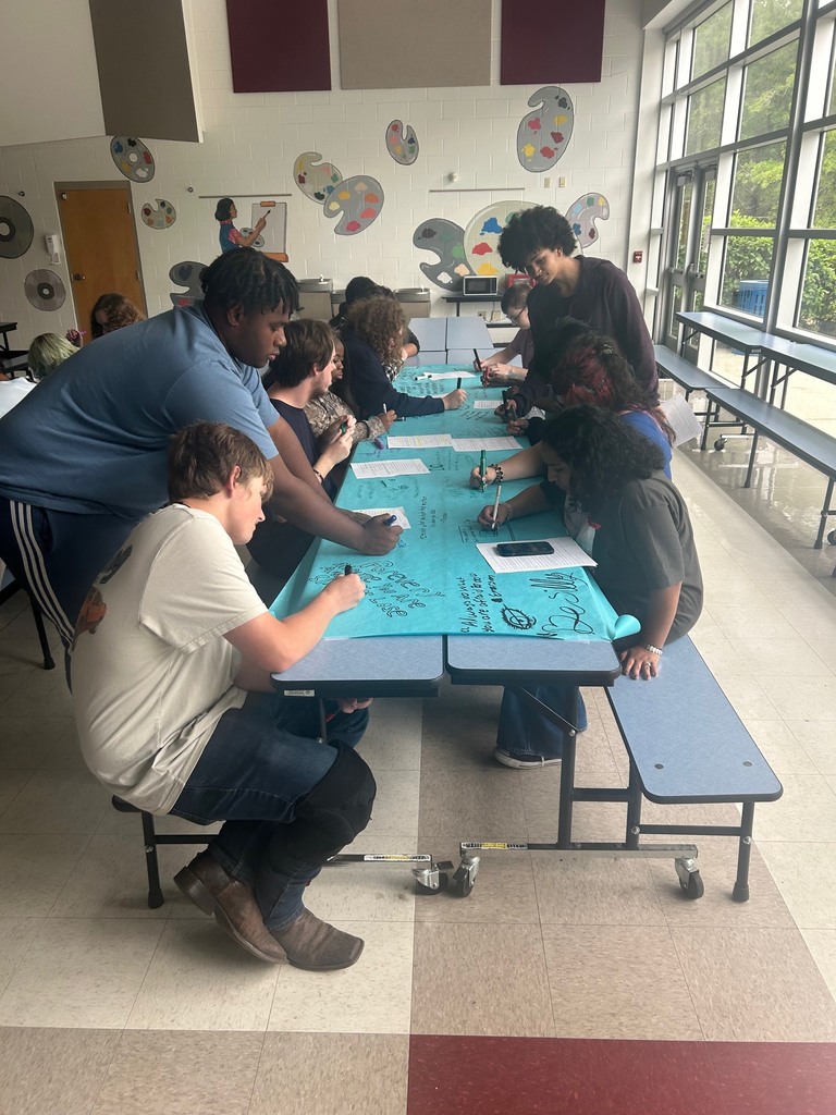 9 students write on large blue bulletin board paper