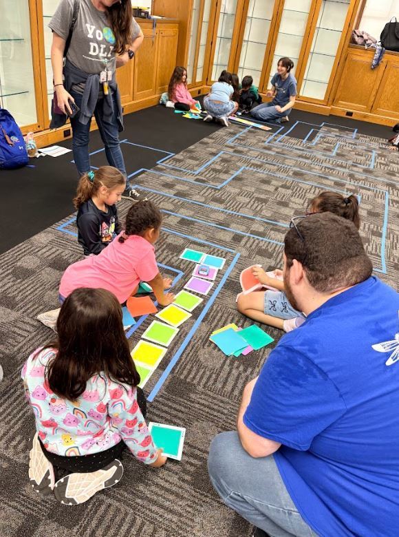 students on the floor working with a toy car and colored square cards