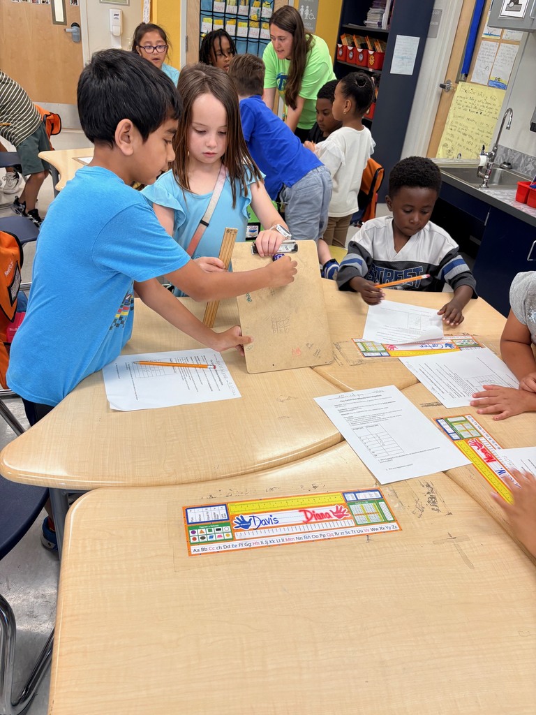 students working at tables with clipboards, toy cars, and rulers