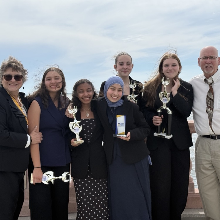 students stand in front of a beautiful blue sky with their trophies 
