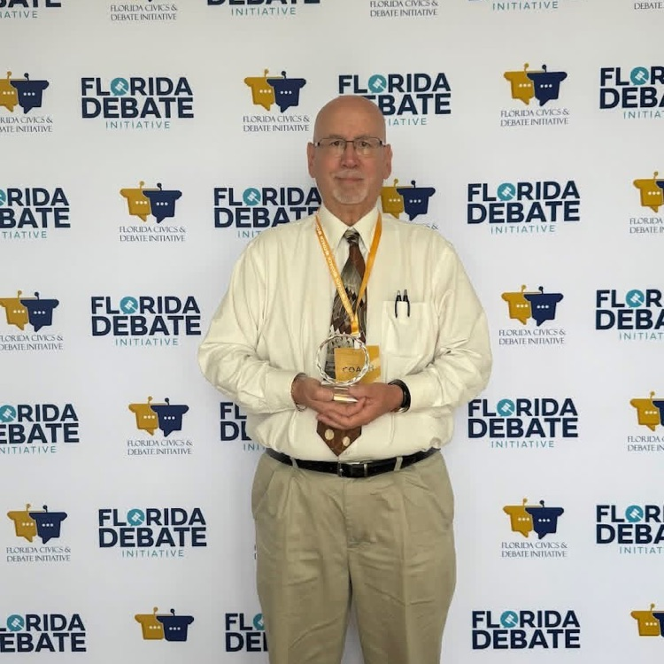 Mr. Barron in front of a Florida debate background with his trophy. 