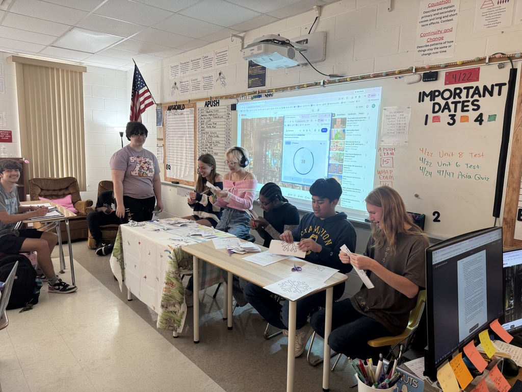 6 students sit a table cutting sheets of paper