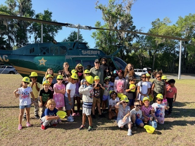 class in yellow hardhats in front of a helecopter