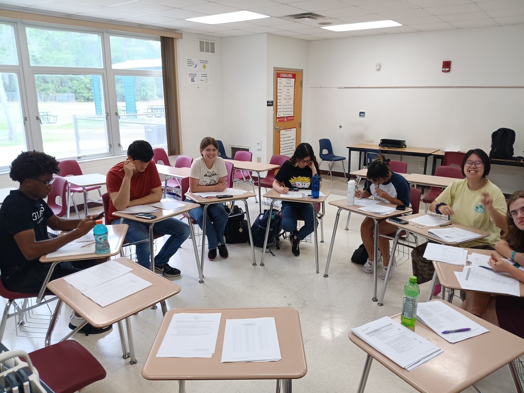 7 students sit at desks that are pushed into a ciricle