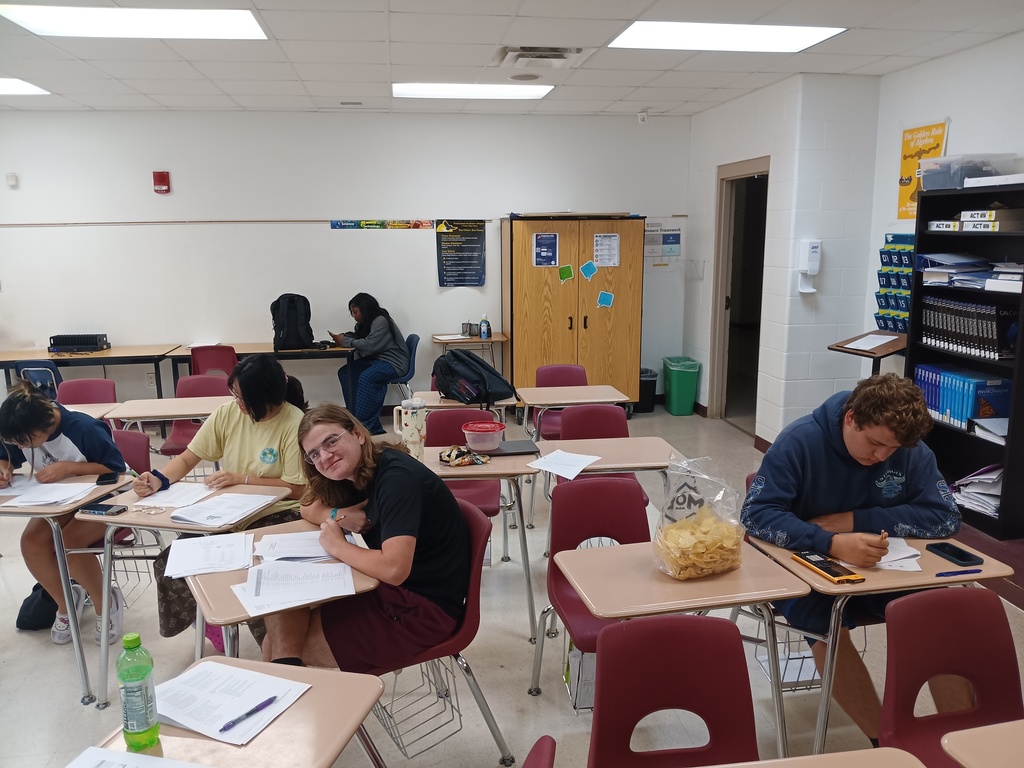3 students look down at their desks and one student looks up and smiles
