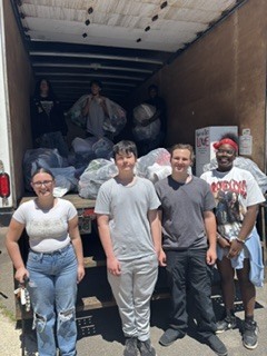 Students stand in front of storage truck holding bags of shoes
