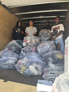 Students stand in a storage trucks loading area with bags of shoes