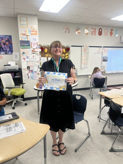 picture of a teacher in a black dress holding a certificate in her classroom