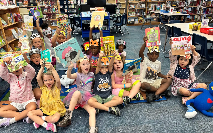 Kindergarten students holding up crocheted bookworms in their books