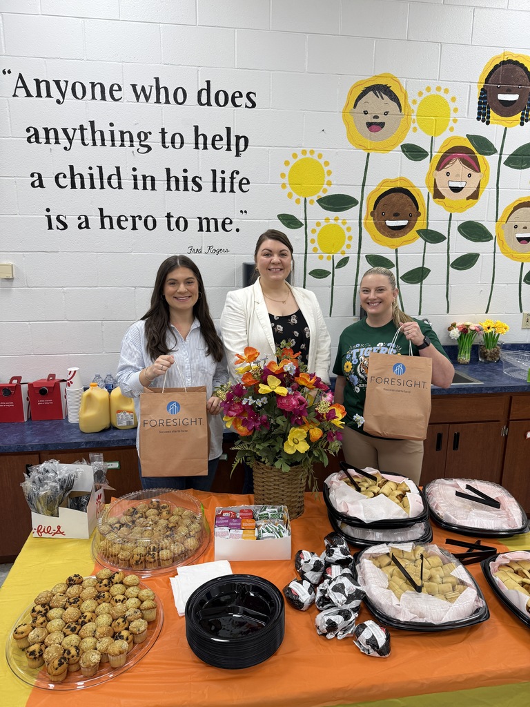 Photo shows two Foresight employees delivering platters of Chick-fil-a breakfast to the principal of Glen Springs Elementary School with swag bags for teachers.