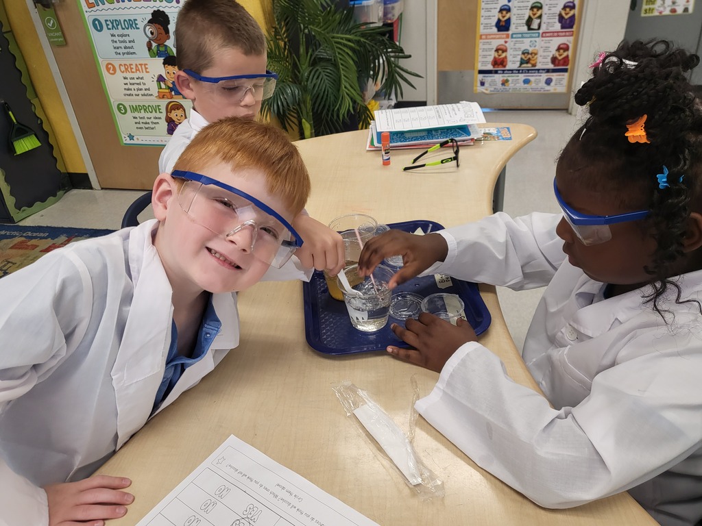 three students in lab coats working at a desk