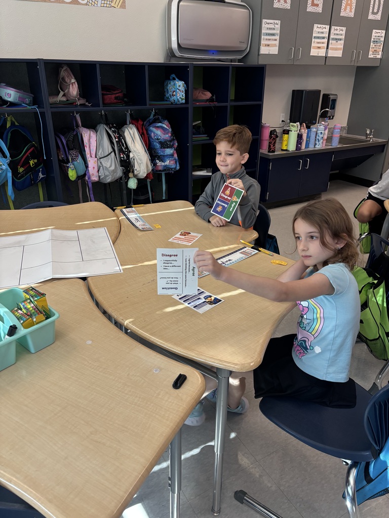 two students at desks holding up cards
