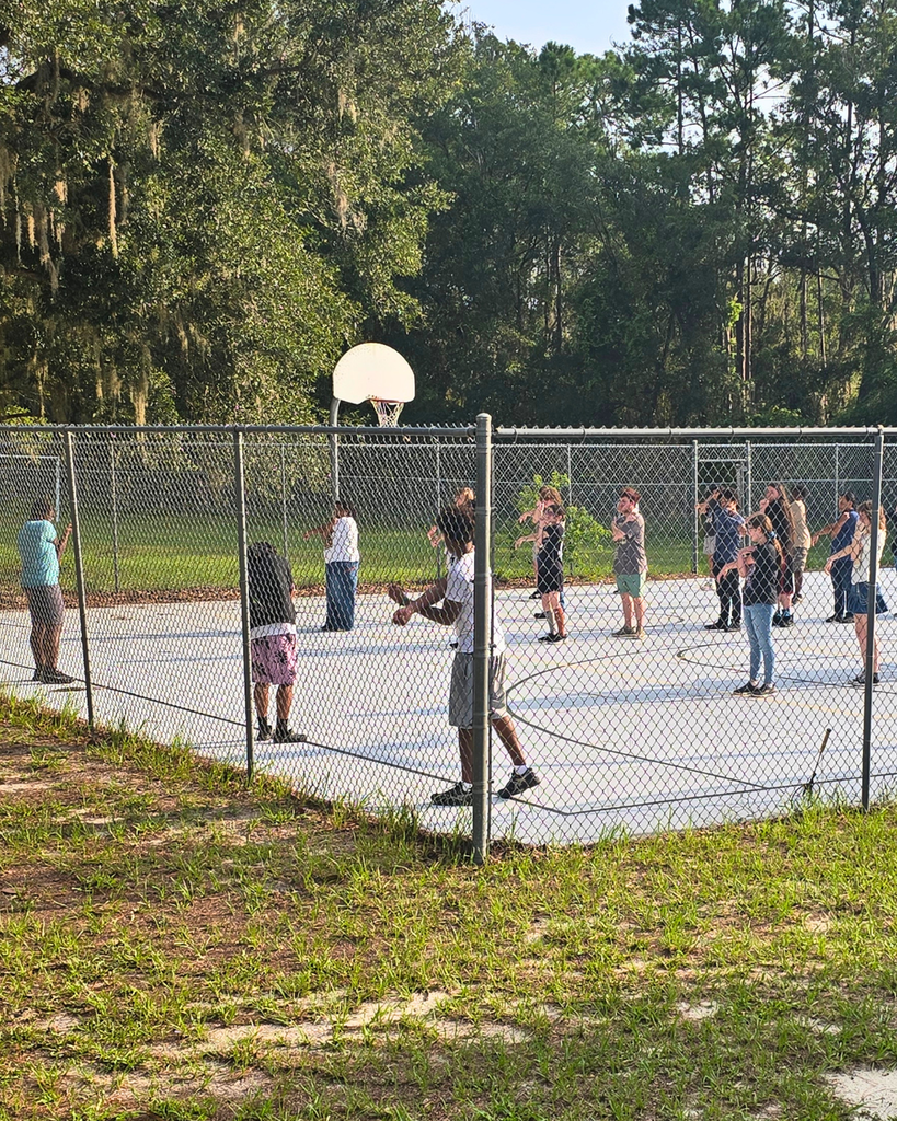 Students stretch their arms across their bodies on the basketball court