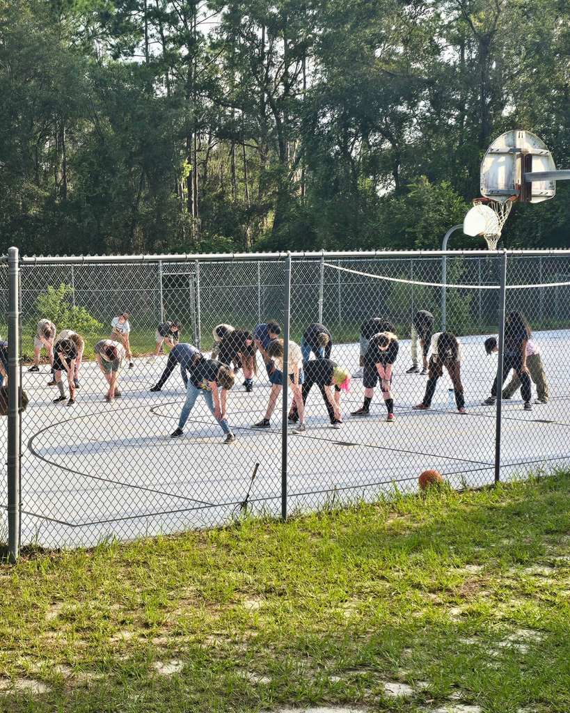 Students touch their toes while standing on a basketball court