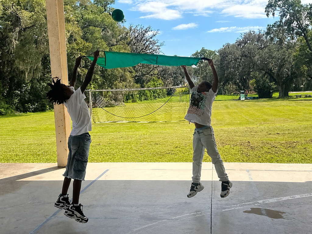 Students working together to catch ball in parachute. 