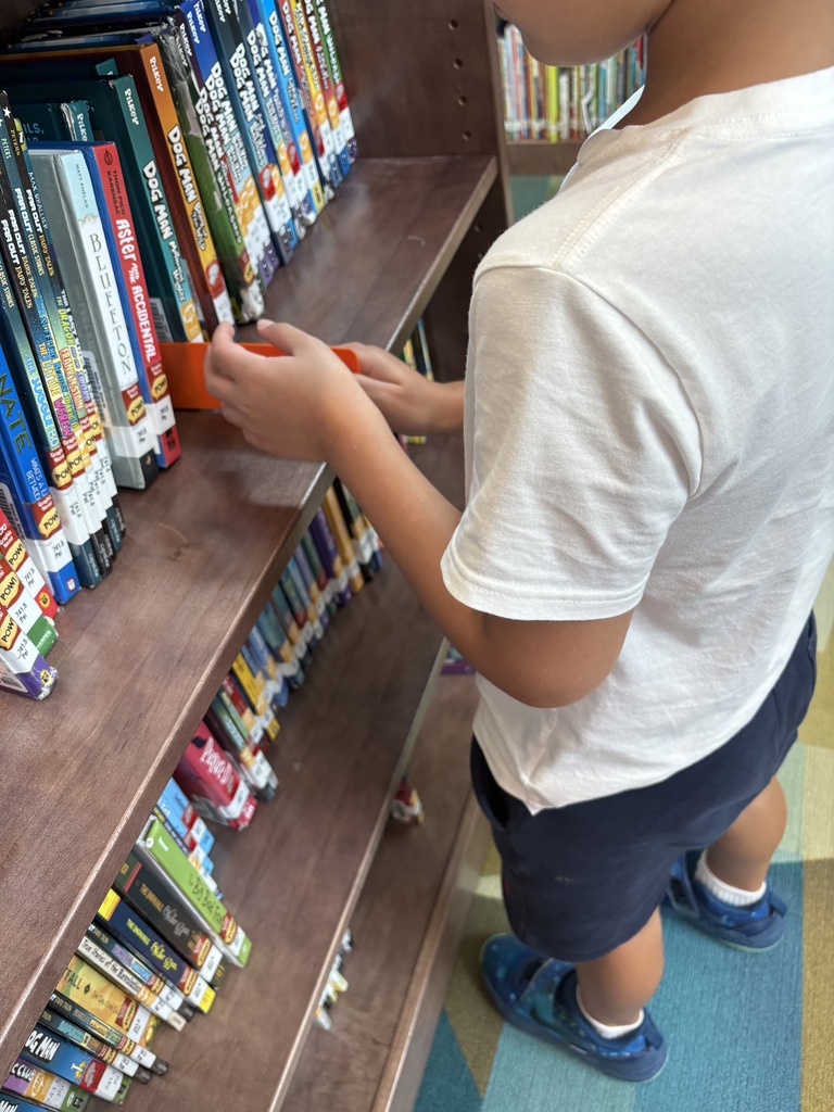 student using a ruler to mark a place on a library book shelf