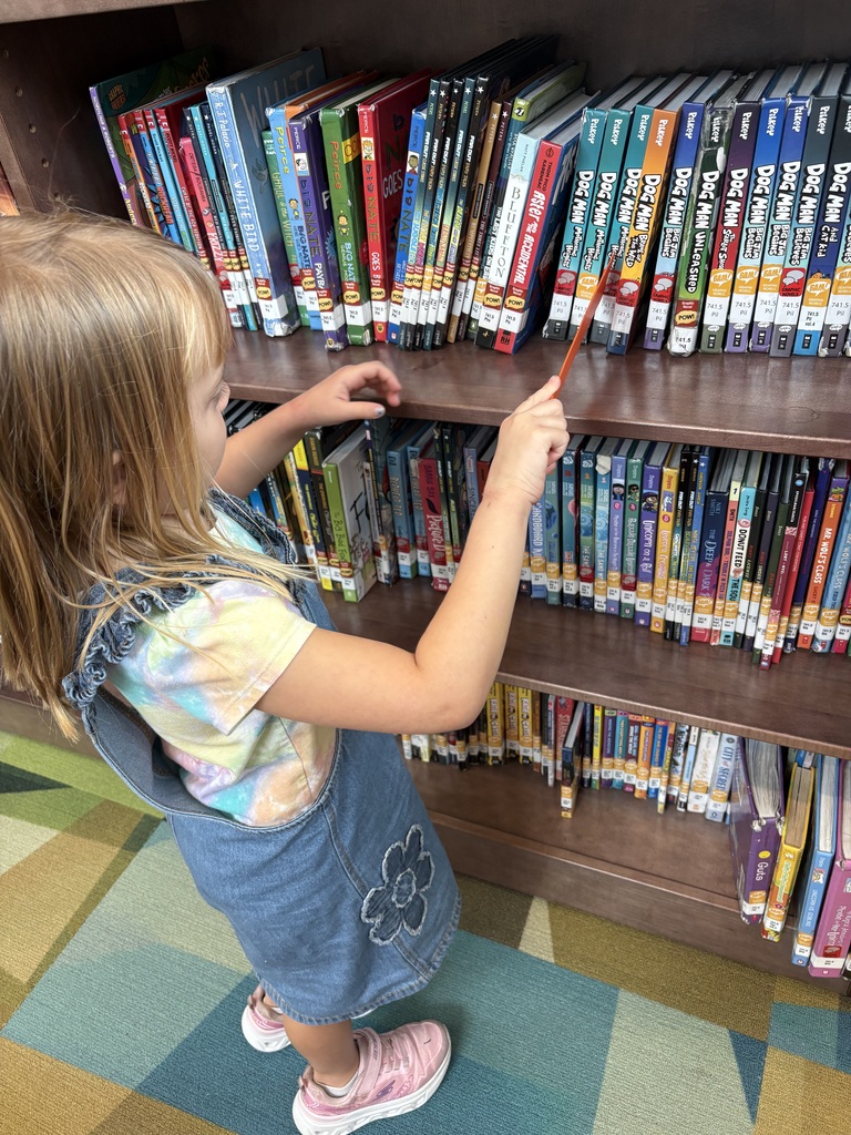 student using a ruler as a marker on a bookshelf to mark her place while looking through library books