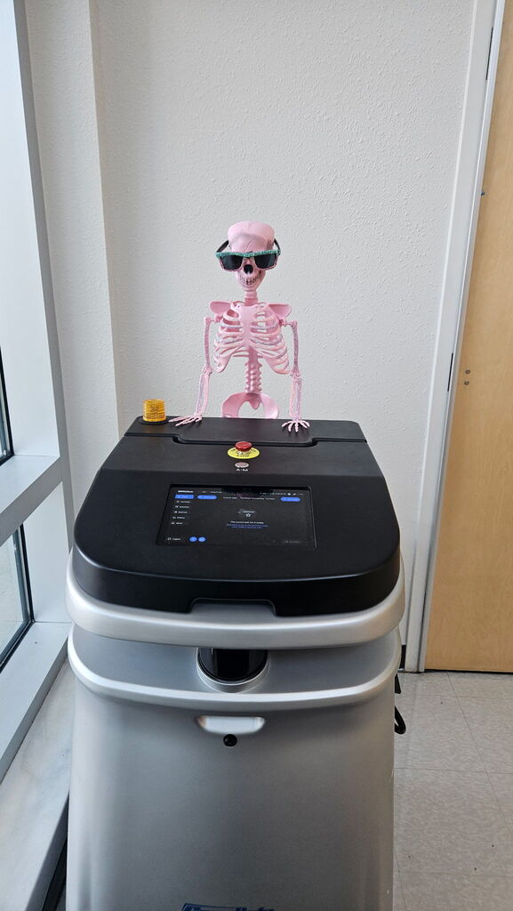 pink skeleton pushing a large silver and black robot vacuum