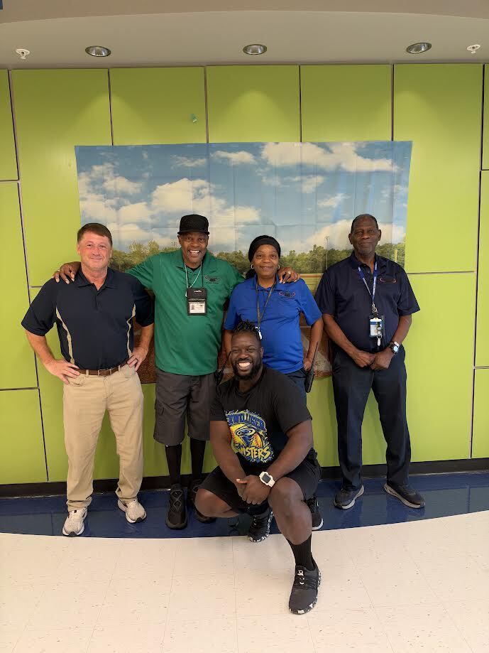 picture of five people smiling together in front of a green wall