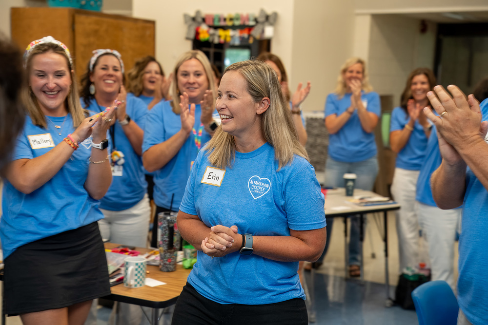 AO Elementary staff clap for Principal Erin Millspaugh in the center of the group. All are wearing blue staff shirts.