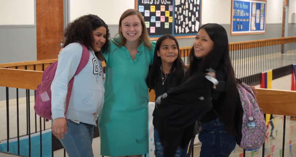 Annie Goldberg wearing a teal dress standing between a group of three teenagers in the hallway at Broadview