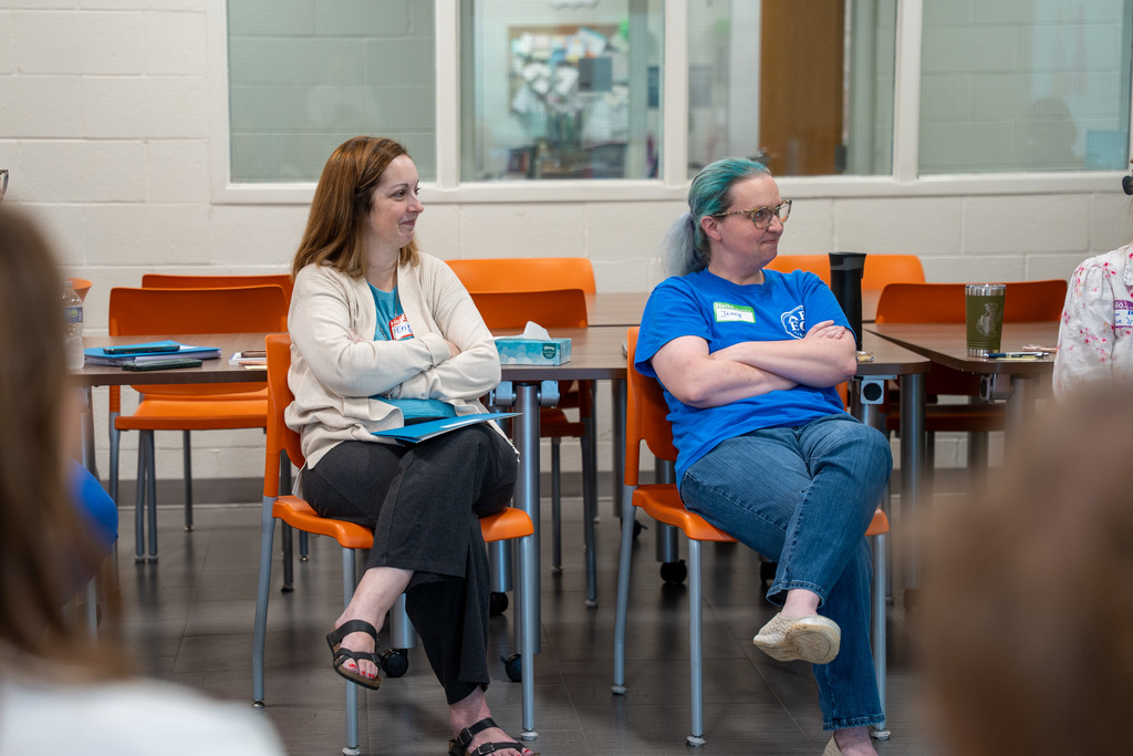 Two teachers sitting in orange chairs with their arms crossed and smiling