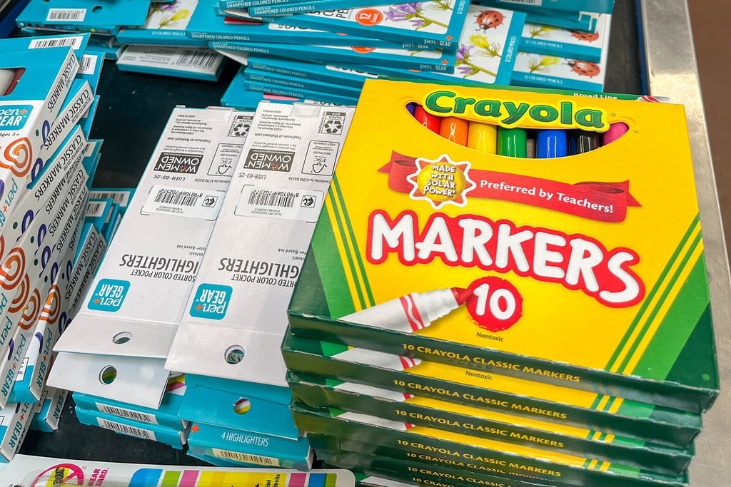 Close-up of school supplies including stacks of Crayola markers, colored pencils, highlighters, and other educational materials organized in shopping cart.