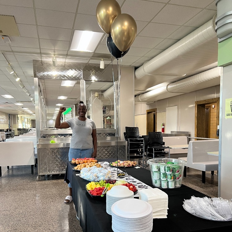breakfast foods on a table with balloons and a lady standing at the end of the table