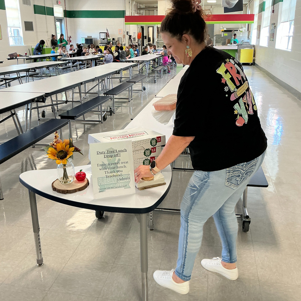 A teacher at Pleasant Grove Elementary wearing a black shirt treats herself to a doughnut on a small table in the school cafeteria