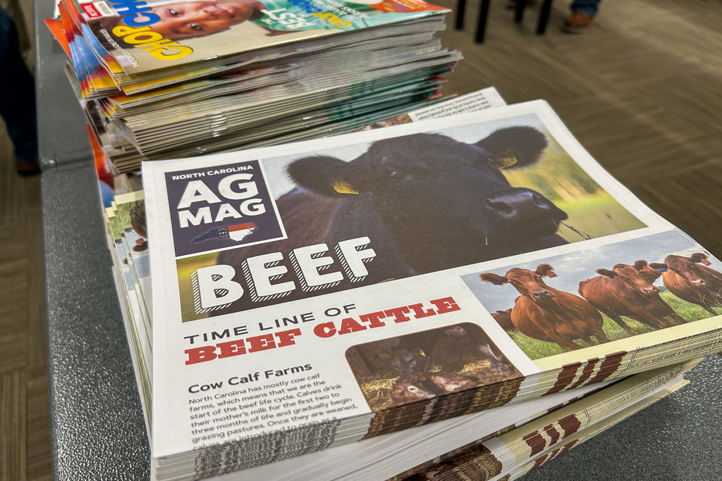 A stack of North Carolina AG MAG publications on a table. The top magazine features a large black cow on the cover with the headline "BEEF: TIME LINE OF BEEF CATTLE" and includes images of cattle in pastures.