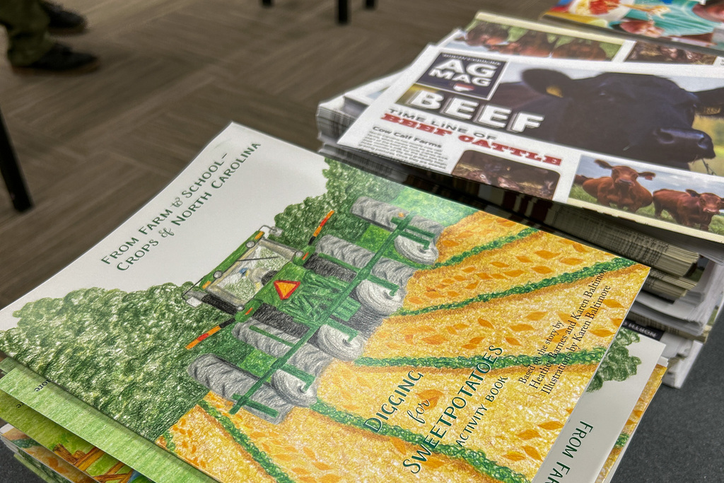An open agricultural education booklet titled "From Farm & School to Crops & North Carolina" displaying colorful illustrations of farm equipment, crops, and agricultural processes across a two-page spread with golden cornfields prominently featured.