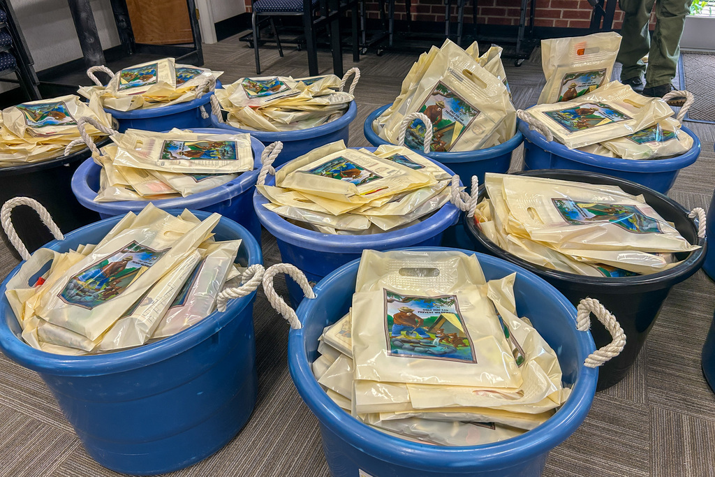 Close-up view of blue plastic bins filled with cream-colored canvas tote bags featuring agricultural education materials. Each bag has rope handles and displays colorful farm-themed graphics on the front.